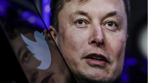 Portraitbild von Elon Musk, dessen Gesicht spiegelt sich in einem Glas mit Twitter-Logo