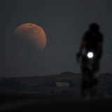 Eine Person fährt in Kalifornien Rad. Im Hintergrund ist ein riesiger Mond zu sehen bei der Mondfinsternis