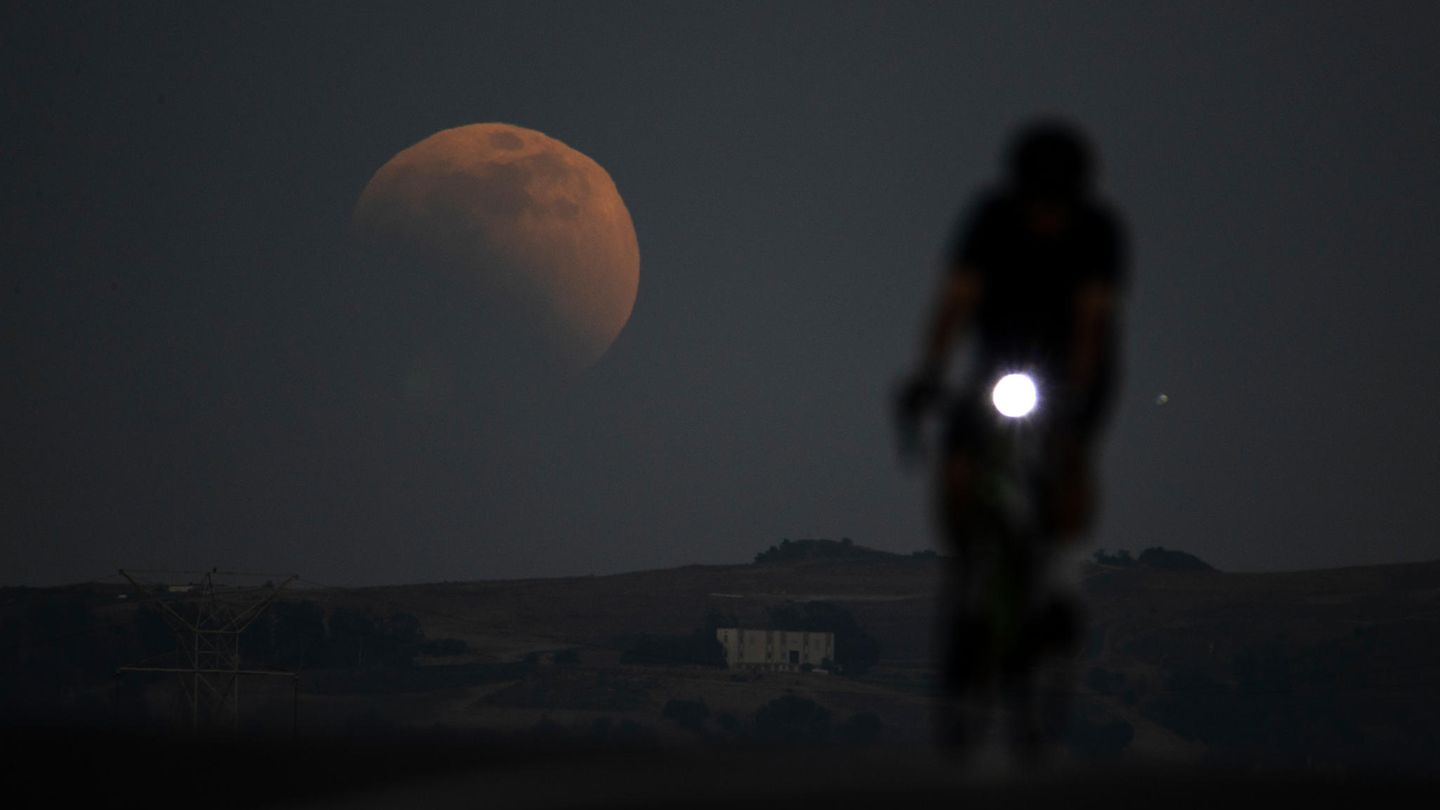 Eine Person fährt in Kalifornien Rad. Im Hintergrund ist ein riesiger Mond zu sehen bei der Mondfinsternis