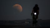 Eine Person fährt in Kalifornien Rad. Im Hintergrund ist ein riesiger Mond zu sehen bei der Mondfinsternis