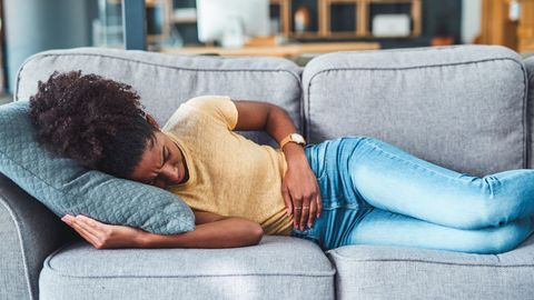 Frau liegt mit Menstrauationskrämpfen auf dem Sofa