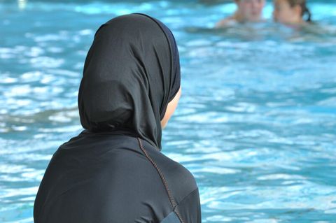 Eine Frau mit einem Burkini sitzt am Rand eines Schwimmbeckens