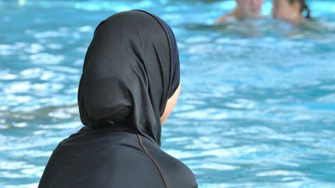Eine Frau mit einem Burkini sitzt am Rand eines Schwimmbeckens
