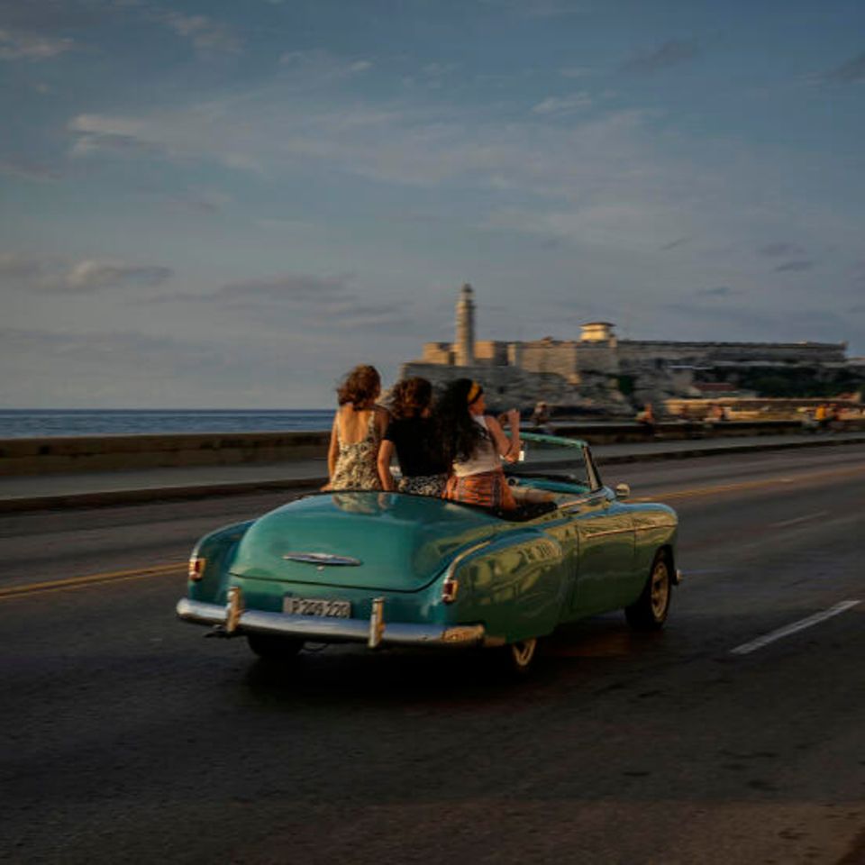 Touristen fahren in einem amerikanischen Oldtimer über den Malecon