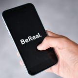 Eine Hand hält ein Handy in der Hand, auf der das Logo der App BeReal zu sehen ist
