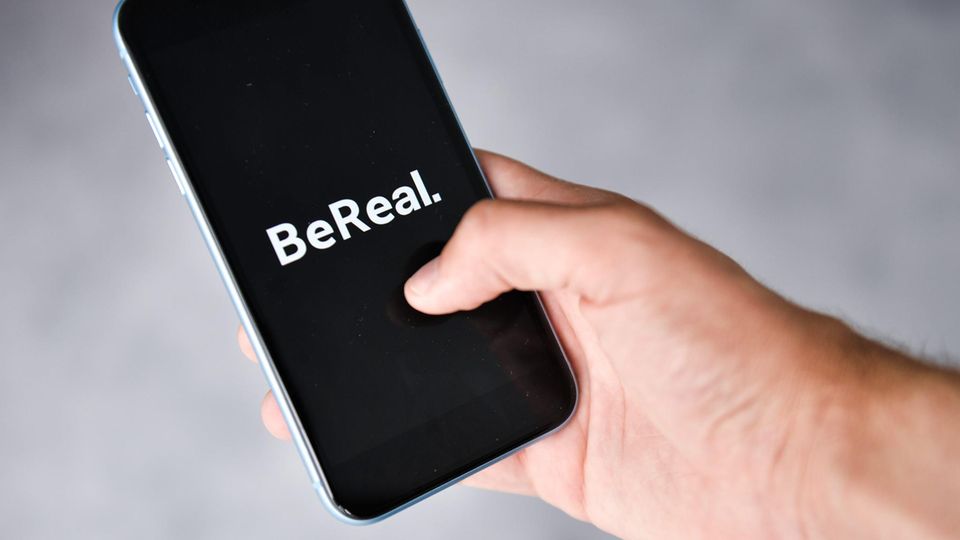 Eine Hand hält ein Handy in der Hand, auf der das Logo der App BeReal zu sehen ist