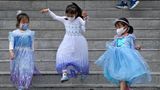 Mädchen in Prinzessinnenkleidern spielen auf einer Treppe und tragen dabei Masken gegen das Coronavirus.