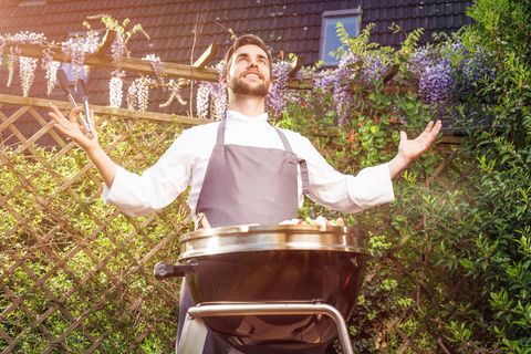 Männer am Grill: Ein Mann erhebt die Hände beim Grillen.