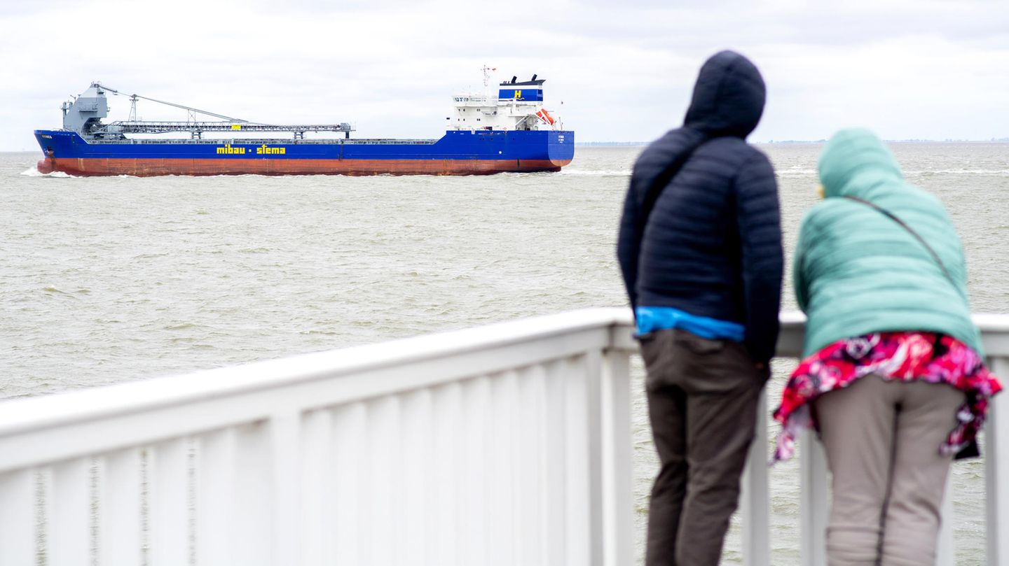 Ein Paar steht bei trübem Wetter am Anleger "Alte Liebe" und verfolgt das Auslaufen eines Frachtschiffes an der Elbmündung