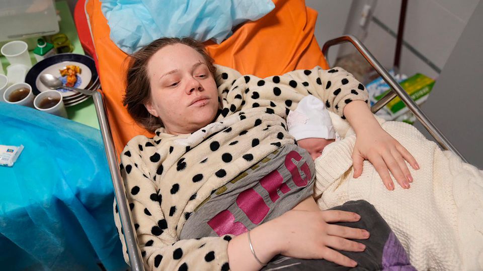 Eine Frau liegt in einem Bett in einer Klinik neben ihrem neugeborenen Baby