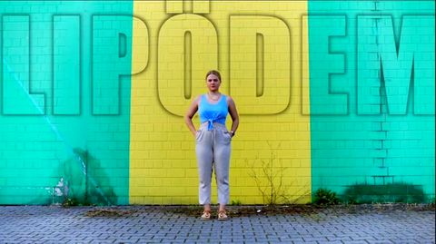 Youtuberin DominoKati steht vor einer Wand – über ihr die Aufschrift "Lipödem"