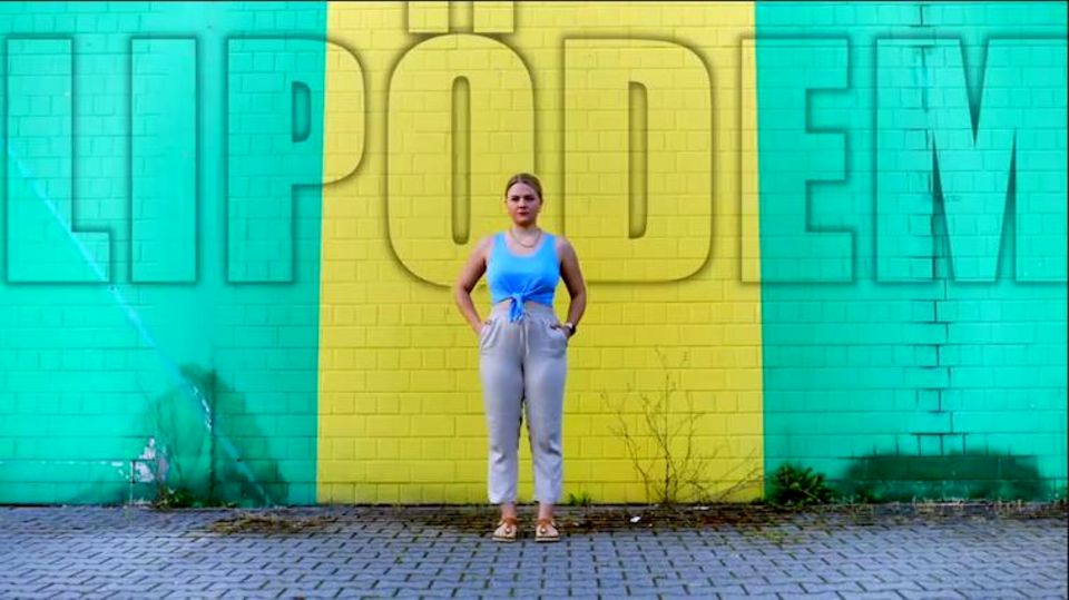 Youtuberin DominoKati steht vor einer Wand – über ihr die Aufschrift "Lipödem"