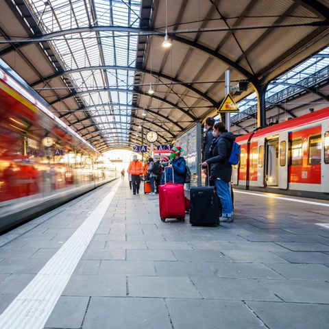 Bahnreisende stehen auf dem Bahnsteig während ein Regionalzug einfährt
