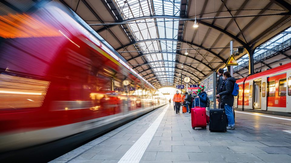 Bahnreisende stehen auf dem Bahnsteig während ein Regionalzug einfährt