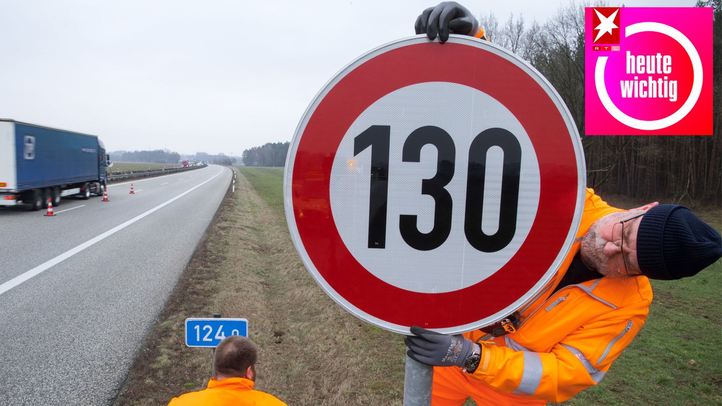 An einer Autobahn montiert ein Mann in leuchtend oranger Arbeitskleidung ein Tempolimit-Schild mit "130" darauf