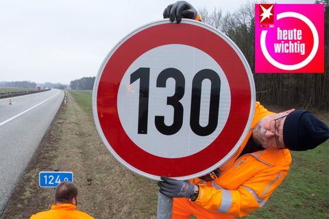 An einer Autobahn montiert ein Mann in leuchtend oranger Arbeitskleidung ein Tempolimit-Schild mit "130" darauf