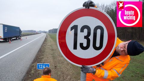 An einer Autobahn montiert ein Mann in leuchtend oranger Arbeitskleidung ein Tempolimit-Schild mit "130" darauf
