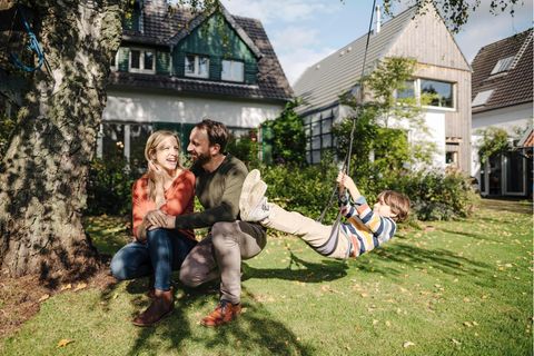 Ein Junge schaukelt im Garten, neben ihm seine Eltern