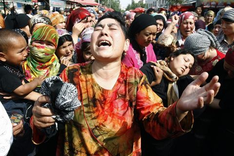 Symbolfoto zu Uiguren: Eine Asiatin in bunt gemustertem Oberteil wirft klagend ihren Kopf zurück und hebt ihre Hände