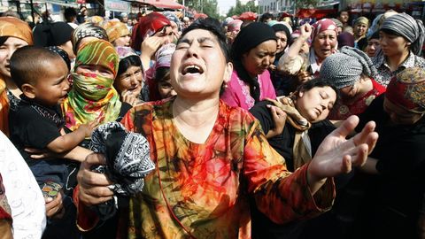 Symbolfoto zu Uiguren: Eine Asiatin in bunt gemustertem Oberteil wirft klagend ihren Kopf zurück und hebt ihre Hände