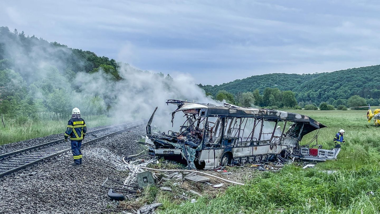 Neben einem Gleisbett bei Ulm steht das ausgebrannte und rauchende Wrack eines Omnibusses auf einer Wiese