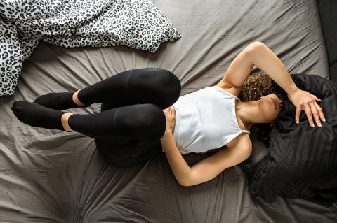 Endometriose: Eine Frau liegt auf dem Bett und hat Schmerzen