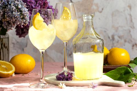 Eine Flasche italienischer traditioneller Likör Limoncello mit Gläsern, Zitronen und eine Vase mit blühendem Flieder