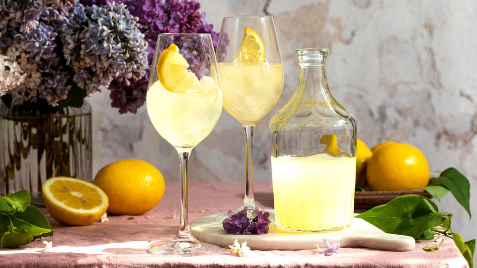 Eine Flasche italienischer traditioneller Likör Limoncello mit Gläsern, Zitronen und eine Vase mit blühendem Flieder