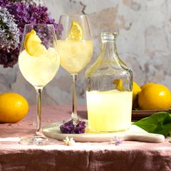 Eine Flasche italienischer traditioneller Likör Limoncello mit Gläsern, Zitronen und eine Vase mit blühendem Flieder