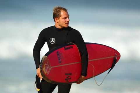 Sebastian Steudtner steht mit seinem Surfbrett unterm Arm am Strand