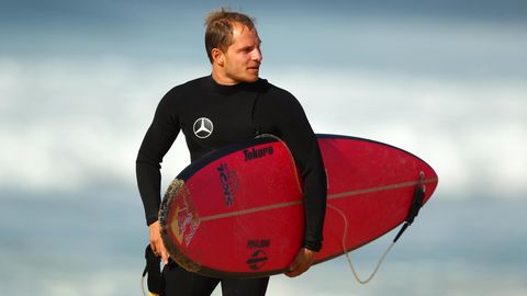 Sebastian Steudtner steht mit seinem Surfbrett unterm Arm am Strand