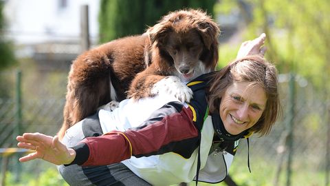 Uta Opel trainiert mit ihrem Rüden Takutai für eine Choreographie in der Sportart Dogdance. Der Hund liegt auf ihrem Rücken.