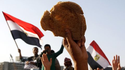 In Ägypten hält ein Demonstrant Brot in die Luft, hinter ihm sieht man Fahnen
