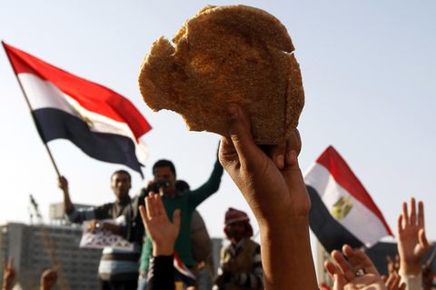 In Ägypten hält ein Demonstrant Brot in die Luft, hinter ihm sieht man Fahnen