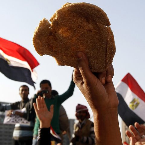 In Ägypten hält ein Demonstrant Brot in die Luft, hinter ihm sieht man Fahnen