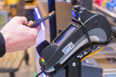 Ein Mann hält ein Smartphone vor ein Kartenterminal der Firma Verifone