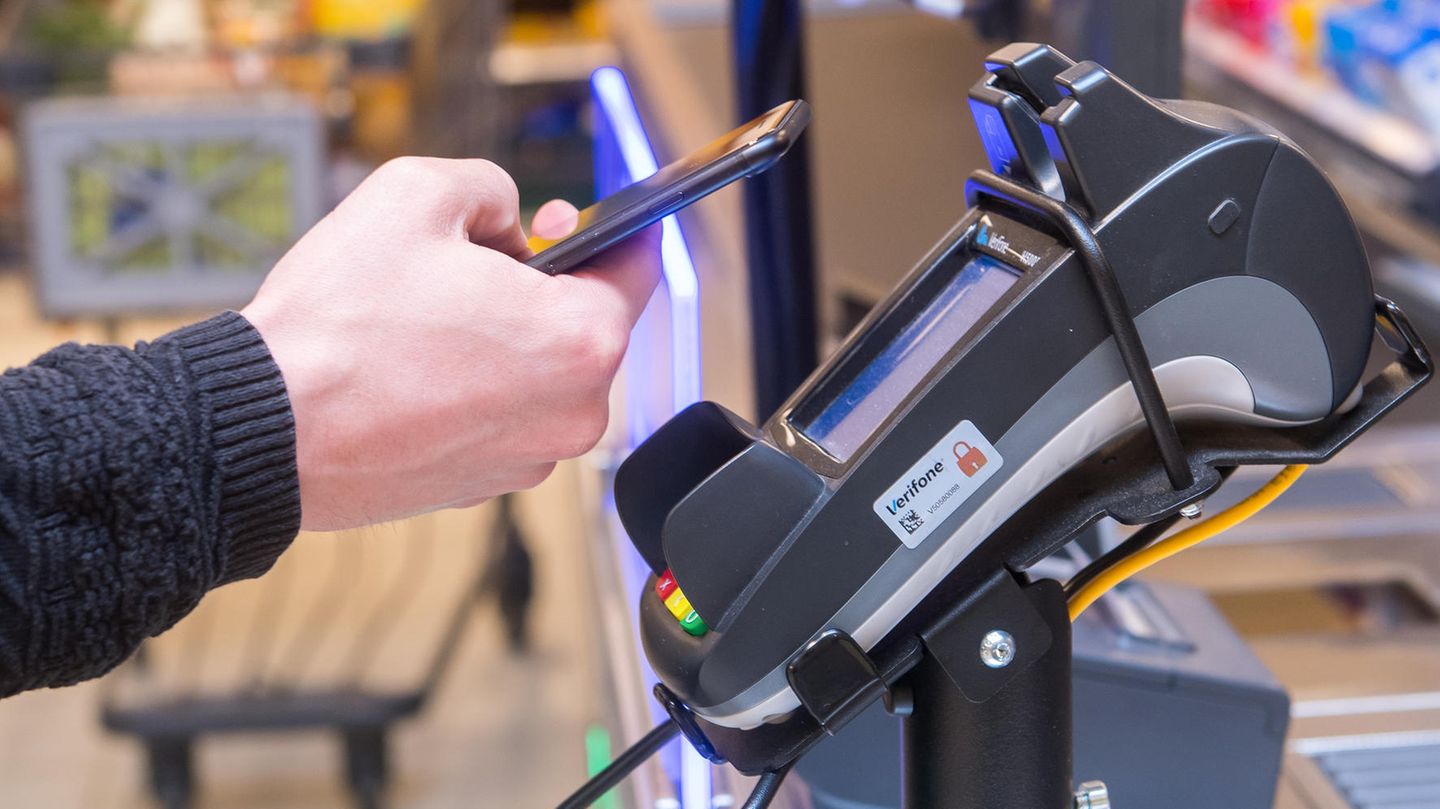 Ein Mann hält ein Smartphone vor ein Kartenterminal der Firma Verifone