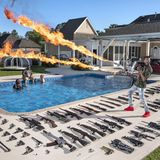 Ein Waffensammler steht vor einem Pool, umgeben von seinen Gewehren und hält einen Flammenwerfer hoch