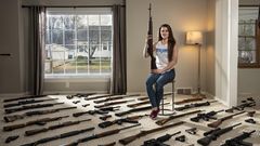 Eine junge Frau sitzt, umgeben von Waffen, in ihrem Wohnzimmer