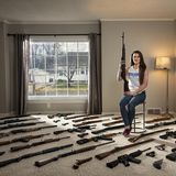 Eine junge Frau sitzt, umgeben von Waffen, in ihrem Wohnzimmer