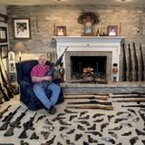 Ein Mann sitzt vor seinem Kamin, das Zimmer ist voller Waffen