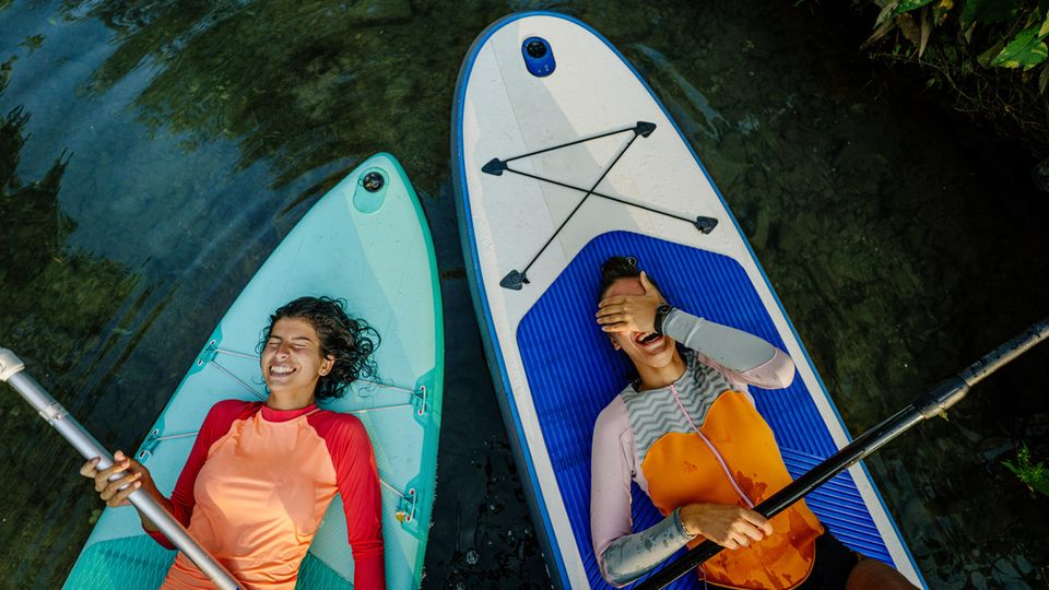 Zwei Frauen liegen auf ihren Stand-Up-Paddle-Boards und lachen.