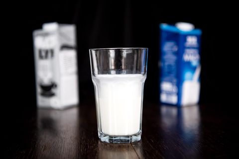 Glas Milch vor zwei Packungen Milch, einer pflanzlichen Milch und einer Kuhmilch