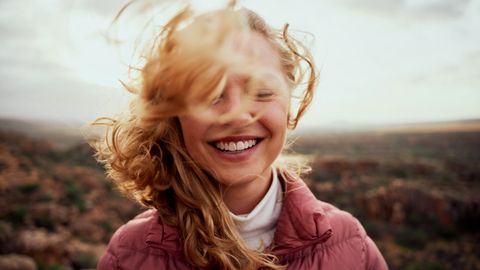 Porträt der jungen lächelnden Frau Gesicht teilweise mit fliegenden Haaren bedeckt in windigen Tag stehend am Berg