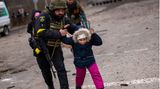 Ein ukrainischer Polizist bringt in Irpin ein Kind vor russischem Artilleriebeschuss in Sicherheit