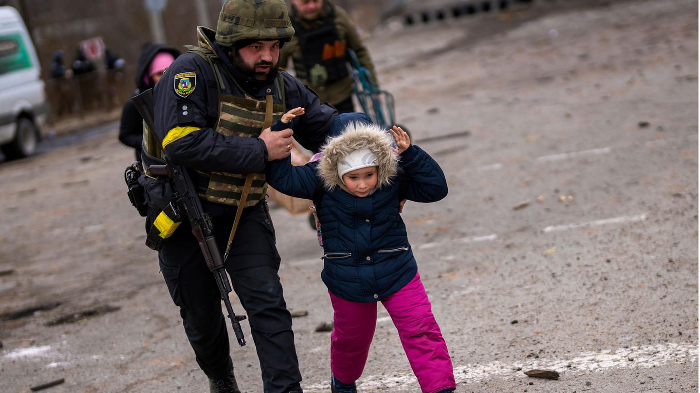 Ein ukrainischer Polizist bringt in Irpin ein Kind vor russischem Artilleriebeschuss in Sicherheit