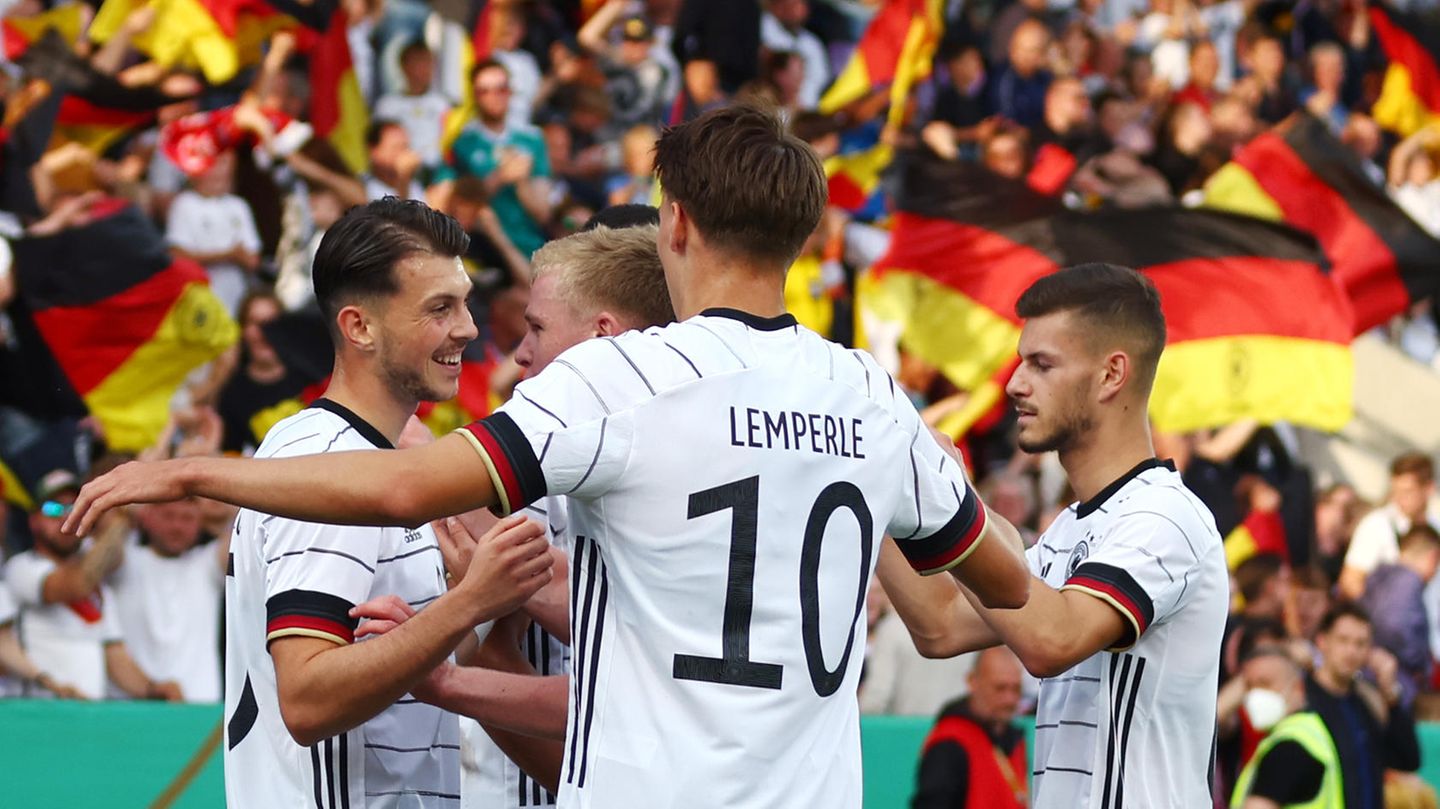 Vier junge Fußballspieler in weißen Trikots und schwarzen Hosen gehen mit ausgebreiteten Armen aufeinander zu und jubeln