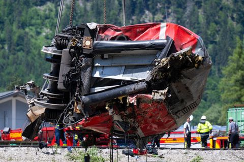 Ein zerbeulter roter DB-Waggon hängt an Drahtseilen über einem Gleisbett