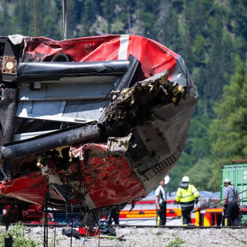 Ein zerbeulter roter DB-Waggon hängt an Drahtseilen über einem Gleisbett