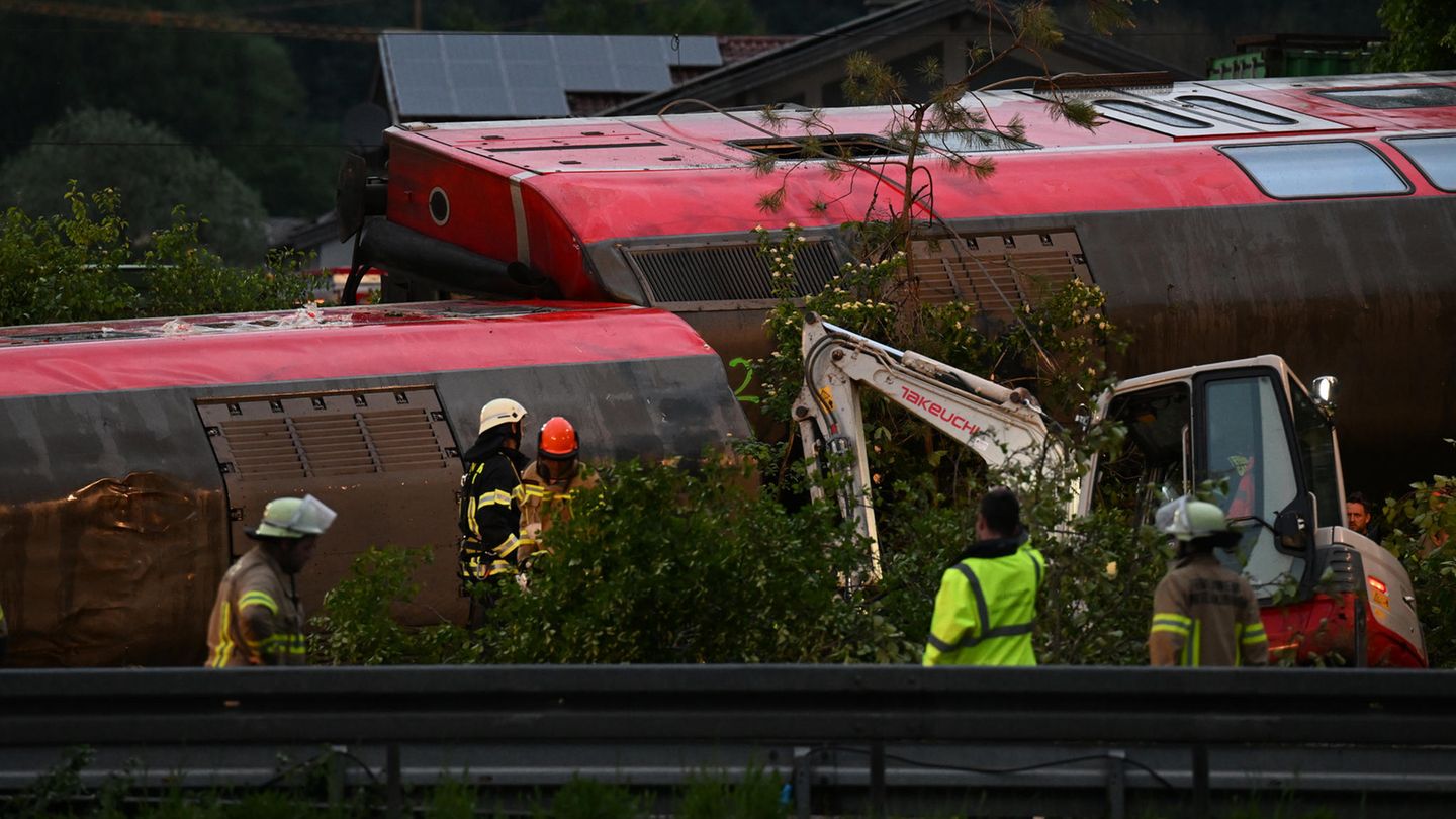 Zwei rote Doppelstock-Waggons liegen in einander verkeilt auf der linken Seite, wodurch die Dächer zu sehen sind